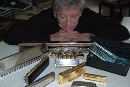 Un harmoniciste accoudé derrière une collection d'harmonicas de toutes tailles